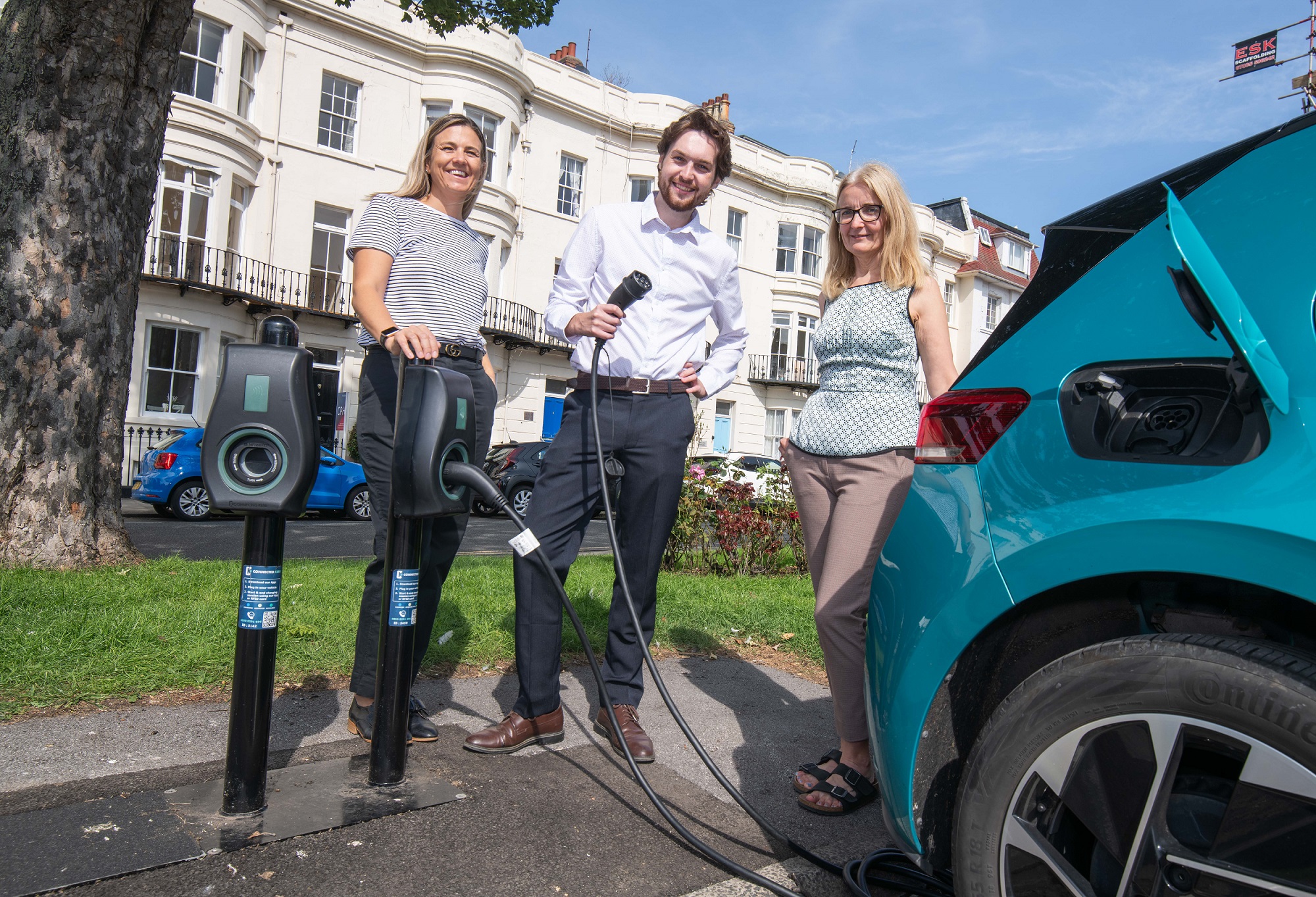 3 people with an electric car and charger
