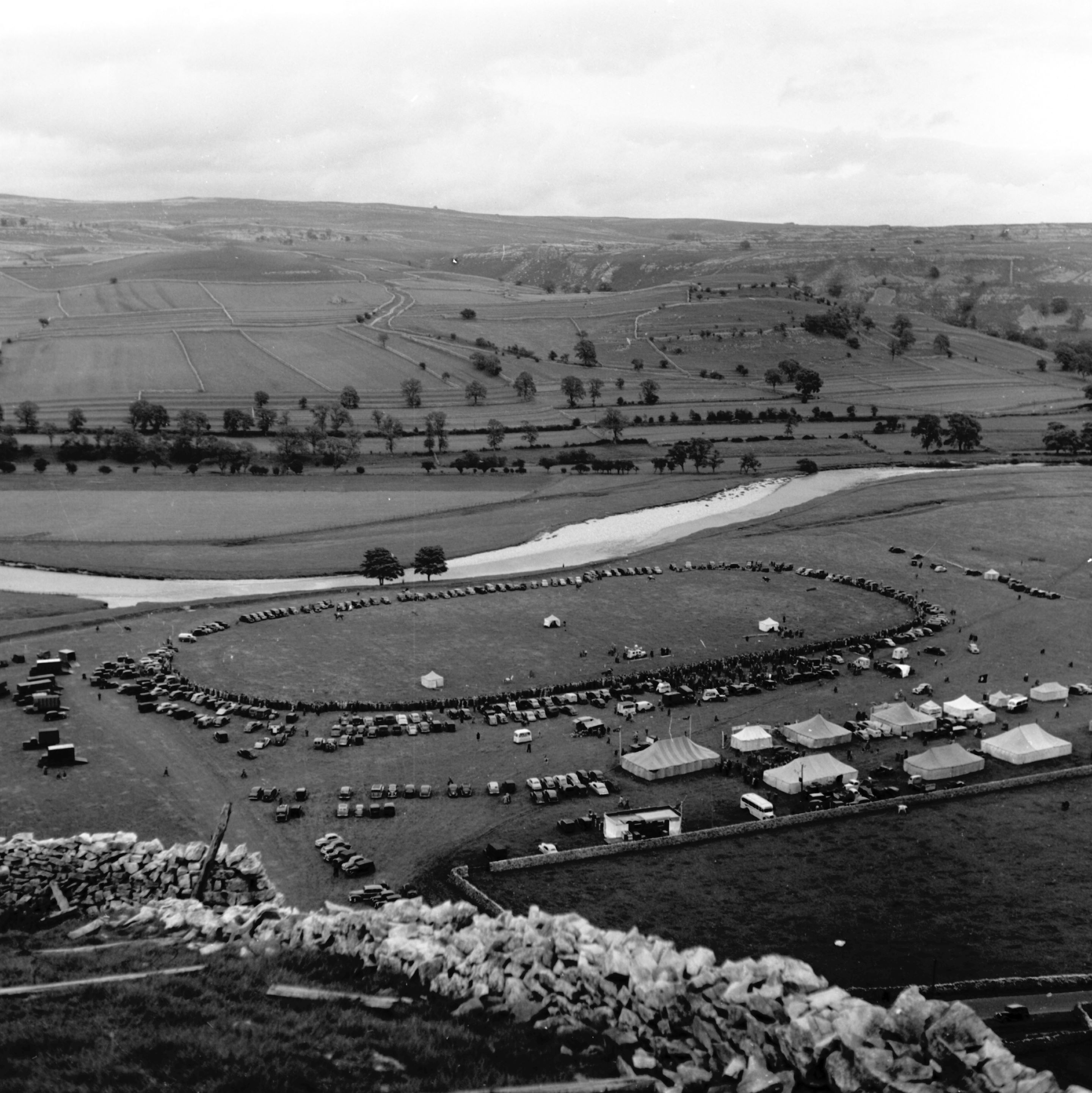 Kilnsey Show is one of the most important agricultural shows in the Yorkshire Dales. The event hosts many activities such as dry-stone walling, sheep dog trials and harness racing. Looking down from the top of Kilnsey Crag, 1950s. From the Bertram Unné photographic collection.