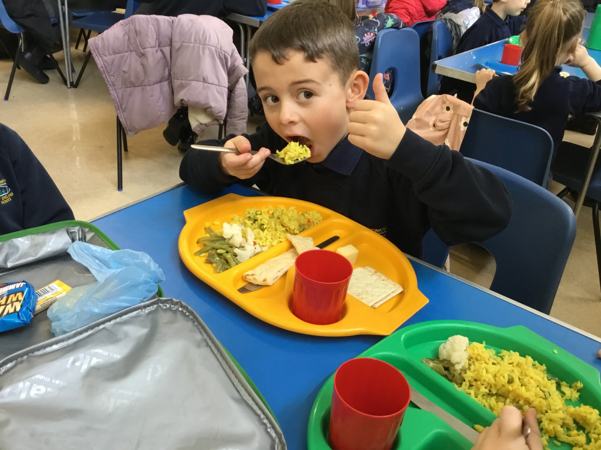 A child eating a school dinner and giving thumbs up