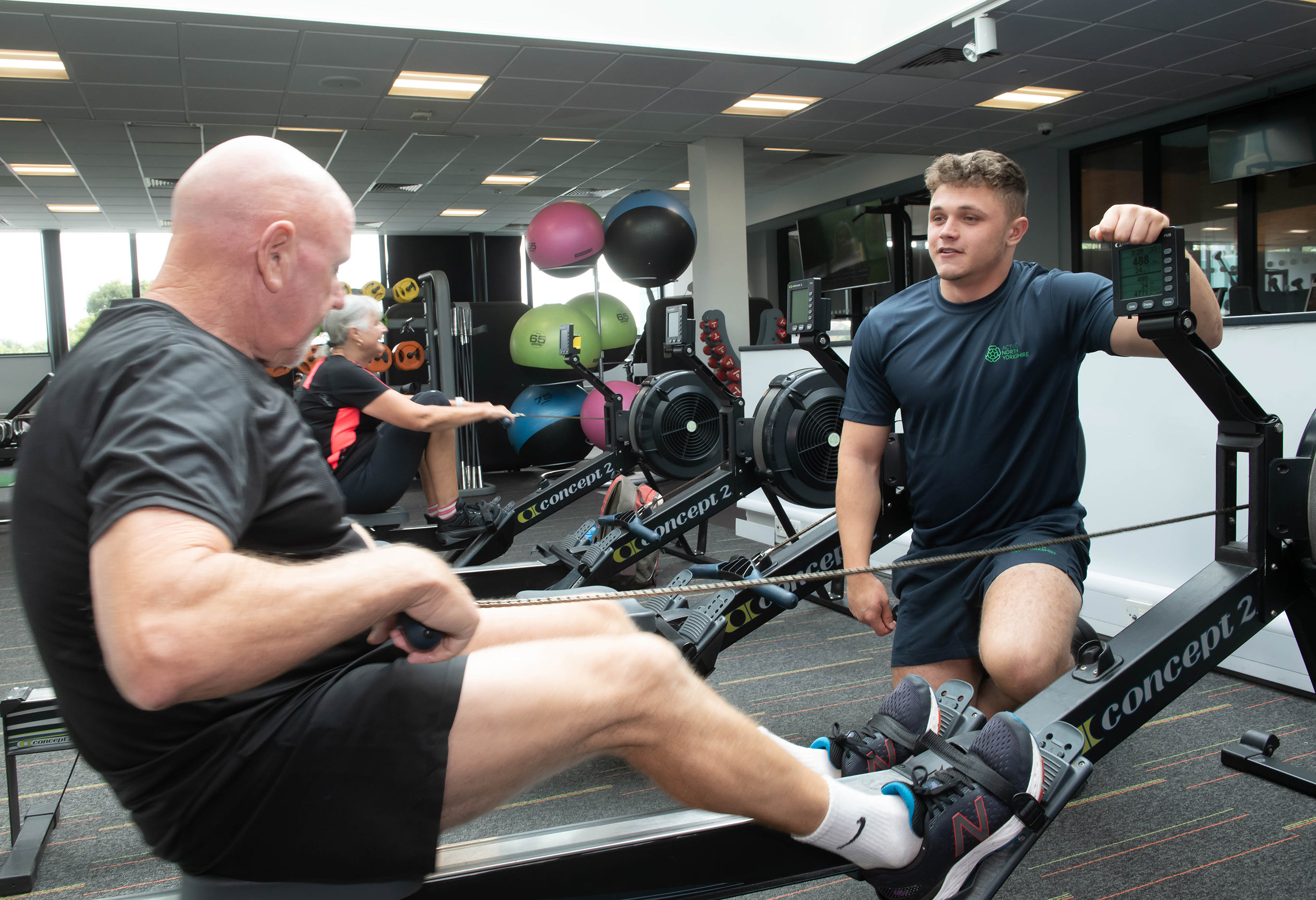 A man on a rowing machine with a gym instructor