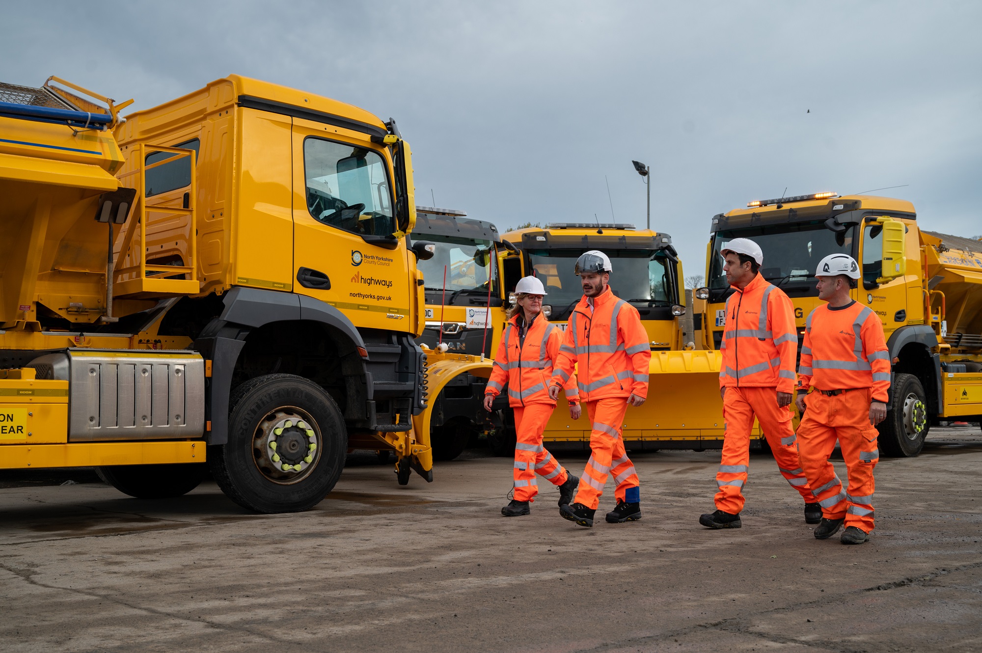 Four gritting crew walking in front of gritters