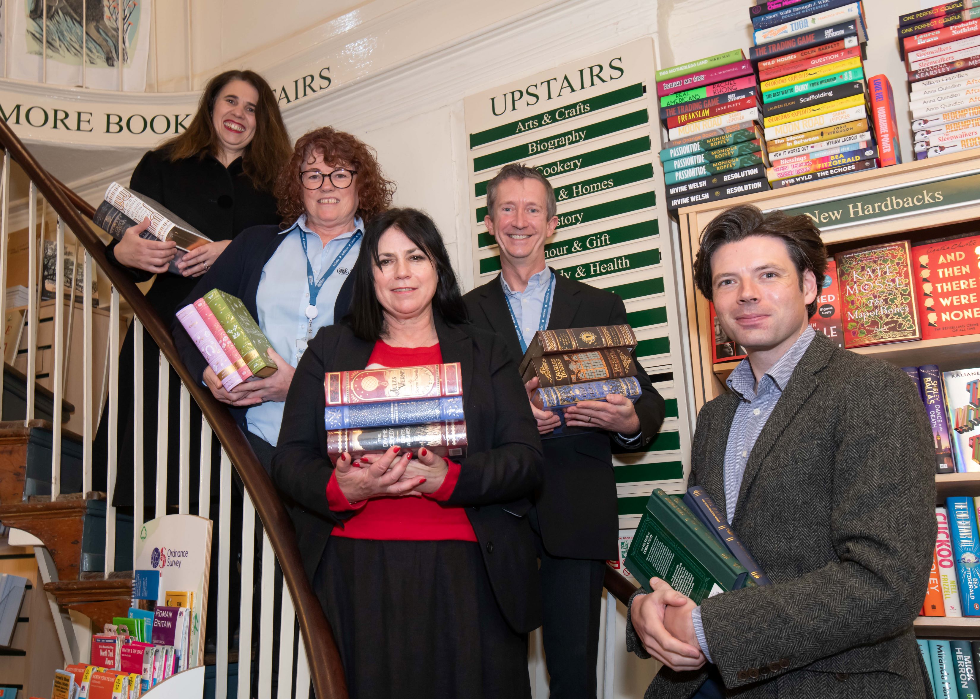 Five people stood on stairs holding piles of books. 