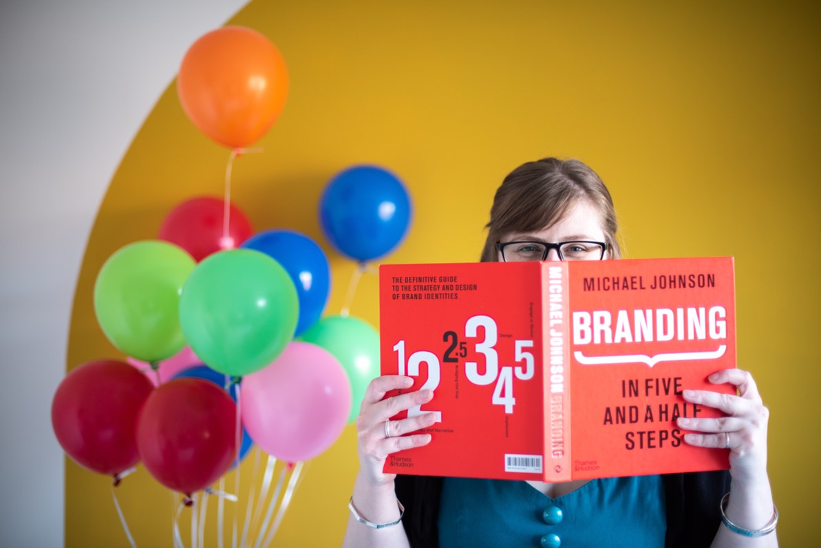 Sian, Graphic Designer, standing by some coloured balloons.