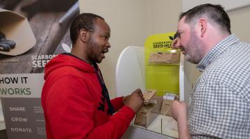 Darren Mancrief, founder and co-chairman of GROW Scarborough, explaining how the seed hub works with library visitor Athenkosi Nyengane