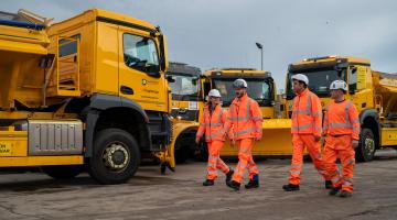 Four gritting crew walking in front of gritters