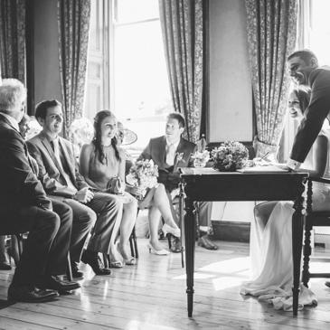 Bride and groom signing the marriage document in front of smiling guests. 
