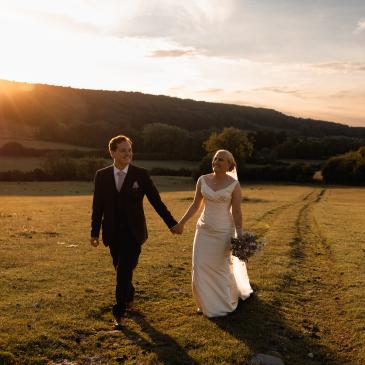 Wedding couple walking through green field during a sunset