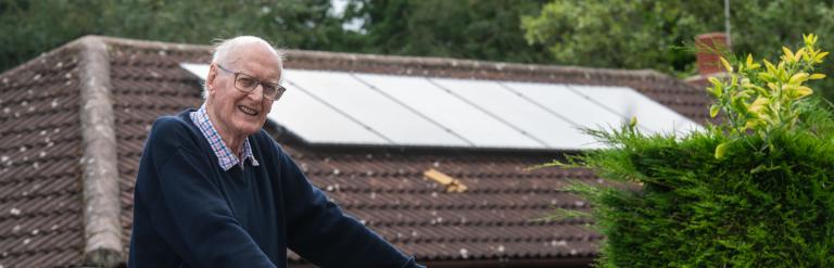 Geoffrey stood in front of his house with solar panels on the roof.