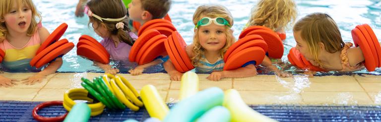 A group of children in the pool wearing arm bands beside a selection of colourful floats