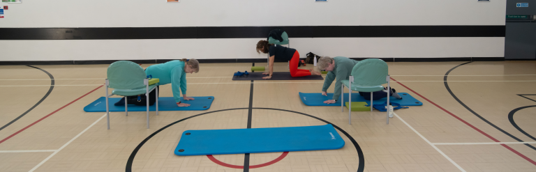 A group of women in yoga poses in the sports hall of the Stockwell Community Wellbeing Hub 